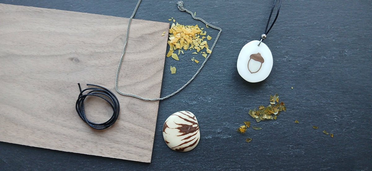 Matières d'un bijou Tagua Lab : noyer, cordon ciré, chaîne en acier 316L, paillettes de carnauba et de gomme laque, tagua brute et pendentif gland